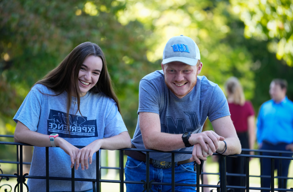 Two students leaning against a rail on campus.